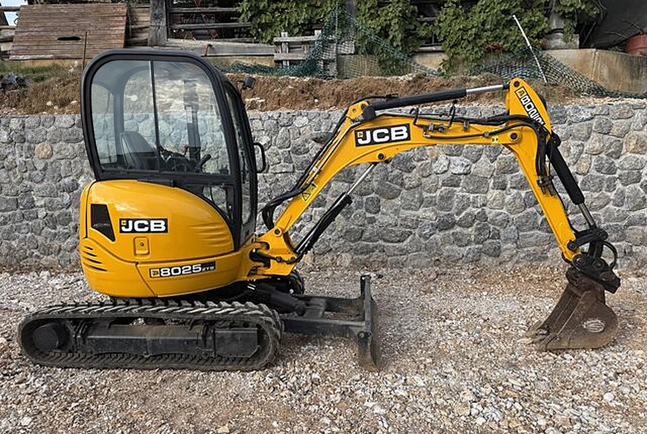 Żółta minikoparka JCB 8025 gąsienicowa z łyżką, zaparkowana na placu roboczym